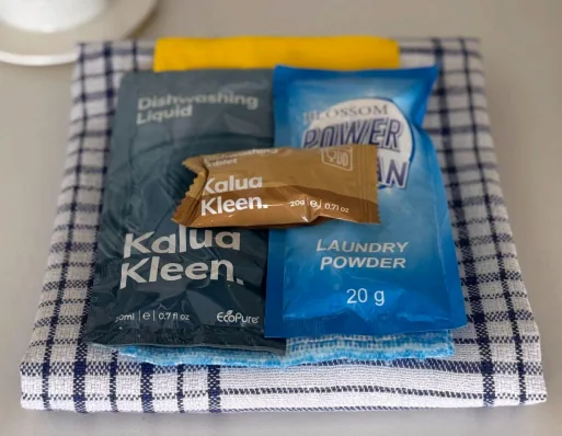 Kitchen amenity pack: dishwashing liquid, a dishwashing tablet and laundry powder on a folded tea towel