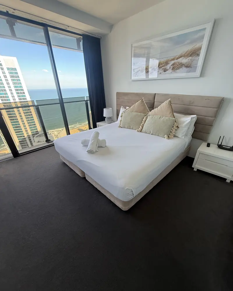 King bed made with white linen and rolled towels in a high-rise apartment overlooking the ocean