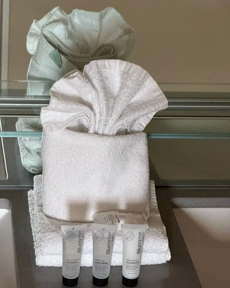 Hand towel folded into a fan beside guest shampoo, body wash and conditioner on a bathroom vanity